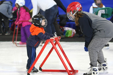 Photo of kids wearing helmets and skates learning ice-skating in a rink
