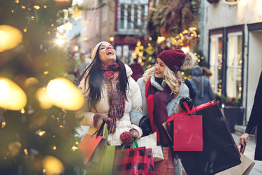 Photo of two women laughing and holding many shopping bags in a street decorated with Christmas trees and lights