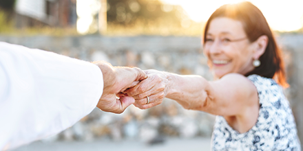 An elderly woman holding her husband's hand, leading him toward a sunrise symbolizing retirement.