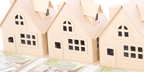 Three cardboard houses, each sitting on a $100 bill, symbolizing real estate investments.