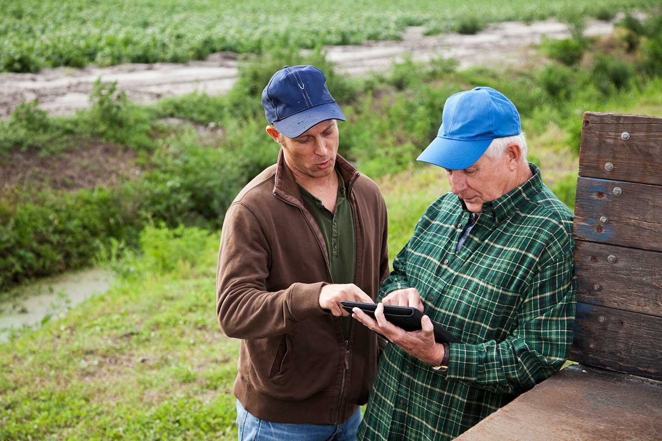 Two farmers, appear to be father and son reviewing materials on ipad. 