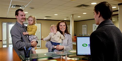 Hannah, her husband and two of their daughters, standing at a teller counter in Servus Credit Union