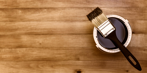 Photo of a paintbrush and a can of paint on a wooden floor