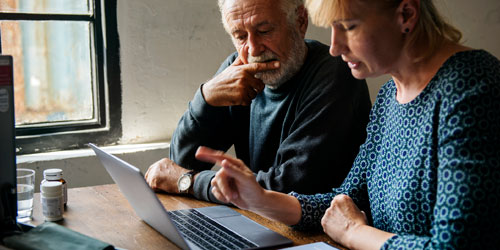 Photo of an elderly person and a younger person both looking at a laptop, thinking about estate planning